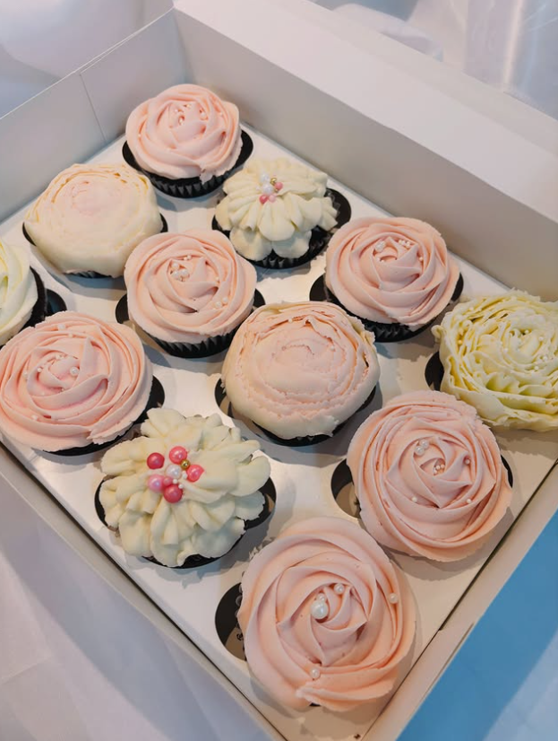 A box of twelve buttercream rose cupcakes in blush and cream